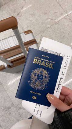 a person holding up a blue and white passport in front of a chair with the word brasil on it