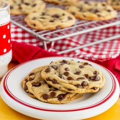 chocolate chip cookies on a plate next to a glass of milk and red checkered tablecloth