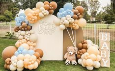 a teddy bear sitting in front of a bunch of balloons on top of a grass field