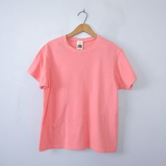 One vintage 1990's plain peach pink tee shirt, men's size small * Crew neckline. * Plain shirt. * Color scheme: pink with peach tones / salmon. | CONDITION | A+. Gently used vintage item. | BRAND | Fruit of the Loom. Made in Honduras. | SIZE | Marked as a child's Large (USA). Fit would be similar to a men's Small or XSmall. PLEASE compare the measurements below to a similar item that fits you for the best sizing! ~ Garment laying flat. Double measurements where applicable. ~ Shoulder width: 15.5 Pink Short Sleeve 90s Style Tops, Basic Plain Pink T-shirt, Basic Pink Plain T-shirt, Peach Relaxed Fit Short Sleeve T-shirt, Casual Plain Pink T-shirt, Peach Tones, Pink Tee Shirt, Plain Shirt, Pink Tee