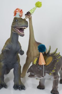 three toy dinosaurs wearing party hats and one dinosaur has a birthday cake on it's head