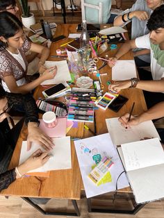 a group of people sitting around a wooden table with notebooks and pens on it