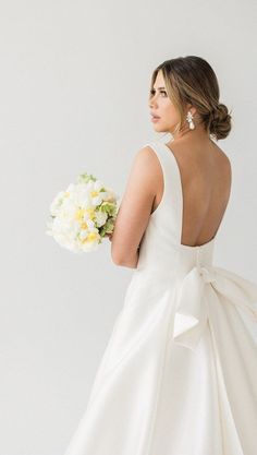 a woman in a white dress holding a bouquet of flowers and looking off into the distance