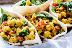 three burritos filled with scrambled eggs and spinach on top of wax paper