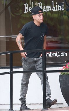 a man in black shirt and jeans walking down the street with his hand on his hip