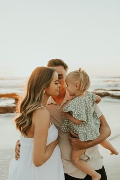 a family standing on the beach at sunset with one child holding his mom and dad