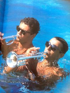 a man and woman in the water playing music on their trombones while wearing sunglasses