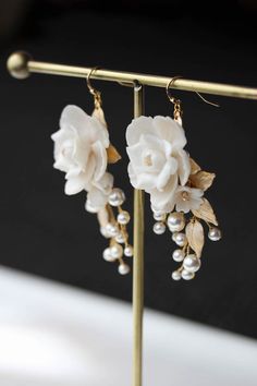 two white flowers and pearls are hanging from a gold stand