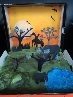 an animal themed cake with blue frosting and trees in the background, on a table