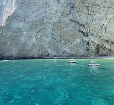 several boats floating in the blue water near a rocky cliff face, with one boat on it's side