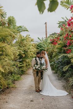 a bride and groom standing in the middle of a path surrounded by tropical plants at their wedding