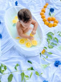 a baby sitting in a bathtub filled with lemons and water surrounded by flowers