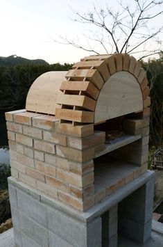 an outdoor brick pizza oven built into the side of a building with trees in the background