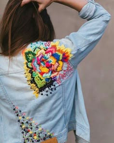 a woman wearing a jean jacket with an embroidered flower on it