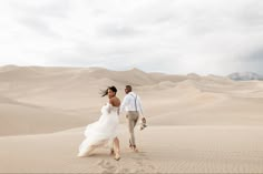 a bride and groom walking through the desert