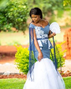 a woman in a blue and white dress is holding a fan while standing on the grass