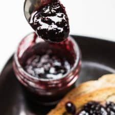 a black plate topped with pancakes covered in blueberry jam and jelly sauce next to a jar of jelly