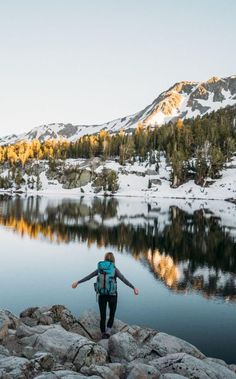 a person with a backpack standing on some rocks by a lake in the middle of mountains