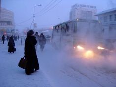 people are walking in the snow next to a bus on a snowy street with steam coming out of it