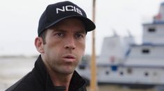 a man wearing a black cap standing in front of a boat