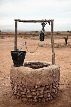 an old stone well with a bucket hanging from it's side in the desert