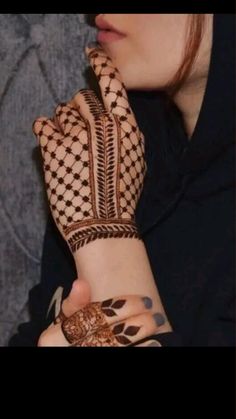 a woman with henna on her arm and hand is holding something up to her face