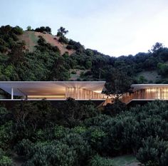 an architecturally designed house sits on top of a hill surrounded by trees and bushes