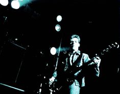 a man standing in front of a microphone and playing an electric guitar at a concert