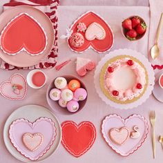 pink and red valentine's day table setting with heart shaped plates, cupcakes, forks, spoons and utensils