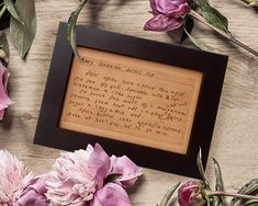 a wooden frame sitting on top of a table with pink flowers and writing in it