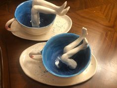 two white figurines sitting inside of blue cups on top of a wooden table