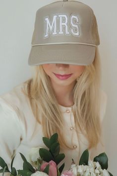 a woman wearing a hat with the word mrs on it and holding flowers in front of her face