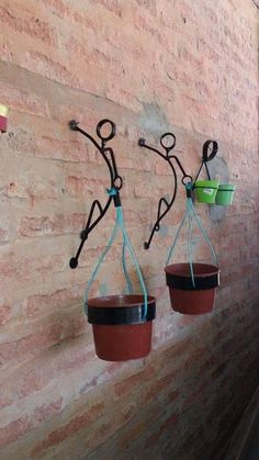 three potted plants hanging from hooks on a brick wall