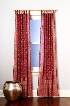 a vase sitting on top of a wooden floor next to a window covered in red curtains