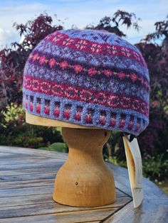 a knitted hat sitting on top of a wooden table next to purple flowers and trees