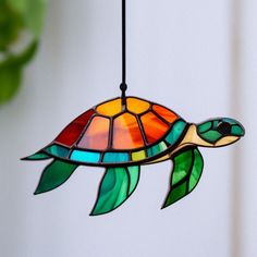 a stained glass sea turtle hanging from a ceiling fixture with green leaves on it's side