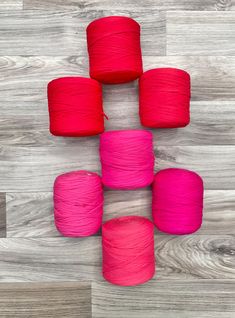 six skeins of pink and red yarn laid out on a wooden floor with wood planks in the background