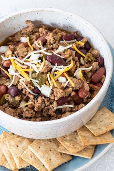 a white bowl filled with chili and cheese next to tortilla chips on a blue plate