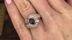 This elegant ring is centered with one (1), bezel set, oval cabochon cut natural sapphire. The sapphire is bordered with eight (8), channel set, tapered baguette cut diamonds and thirty-two (32), bead set, round brilliant cut diamonds. The ring measures 17.0mm at the top, rises 9.7mm above the finger, tapering to 3.8mm wide and 2.0mm thick at the base of the shank. This ring is currently a size 6. Blue Sapphire Diamond Ring, Blue Sapphire Diamond, Bead Set, Sapphire Diamond Ring, Baguette Cut Diamond, Channel Set, Elegant Ring, Baguette Cut, Natural Sapphire