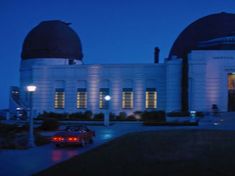 two cars parked in front of a large building with dome lights on it's sides