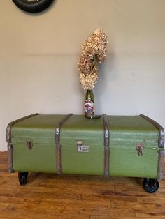 a green suitcase sitting on top of a wooden floor next to a vase with dried flowers