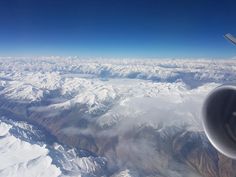 the view from an airplane window shows snow covered mountains and blue sky in the background