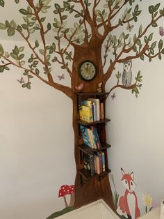 there is a book shelf with books on it and a tree painted on the wall