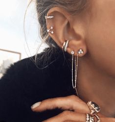 a close up of a person wearing ear rings and chain bracelets on their fingers