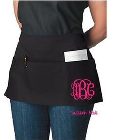 a woman wearing a black apron with pink monogrammed initials on the front and back