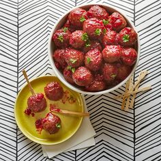 a bowl filled with meatballs and chopsticks next to a yellow plate on a patterned tablecloth