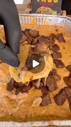 a person in black gloves is scooping some food into a pan with meat and cheese