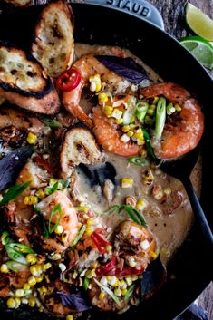 a skillet filled with shrimp, corn and bread on top of a wooden table