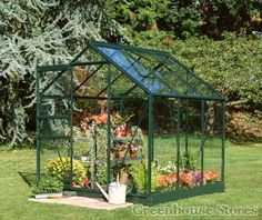 a small green house sitting in the middle of a yard filled with flowers and plants