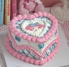 a pink teddy bear sitting on top of a heart - shaped cake in the shape of a box